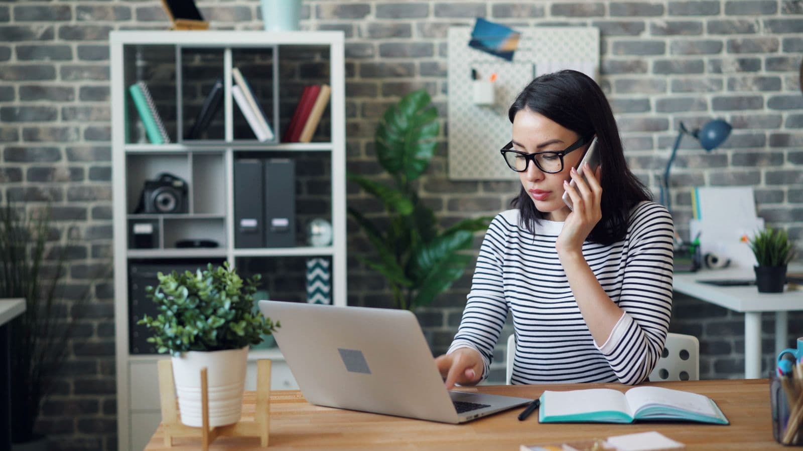 Office receptionist handling a customer call while working on a laptop